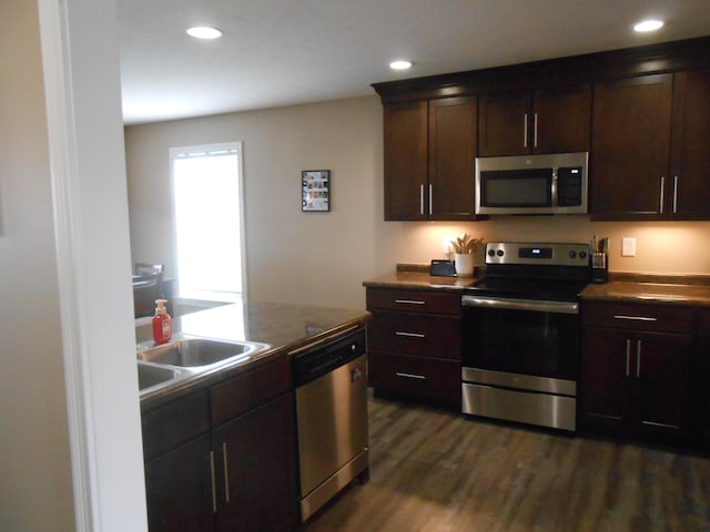 kitchen with stainless steel appliances, dark brown cabinets, sink, and dark wood-type flooring