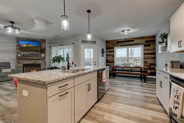 kitchen with a fireplace, a sink, light wood-type flooring, light stone countertops, and black appliances