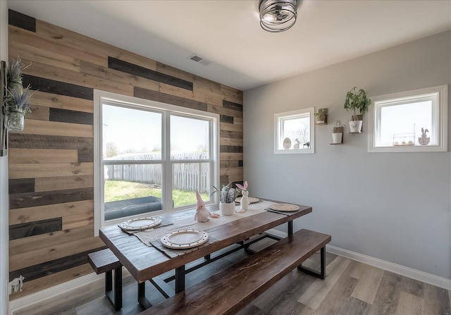 dining space featuring visible vents, plenty of natural light, wood walls, and light wood finished floors