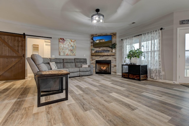 living room featuring wood finished floors, visible vents, a stone fireplace, and a barn door