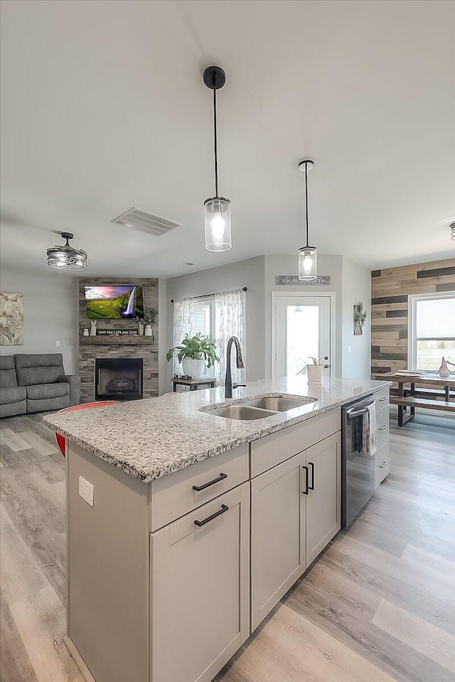 kitchen featuring light stone counters, dishwasher, a stone fireplace, and a sink