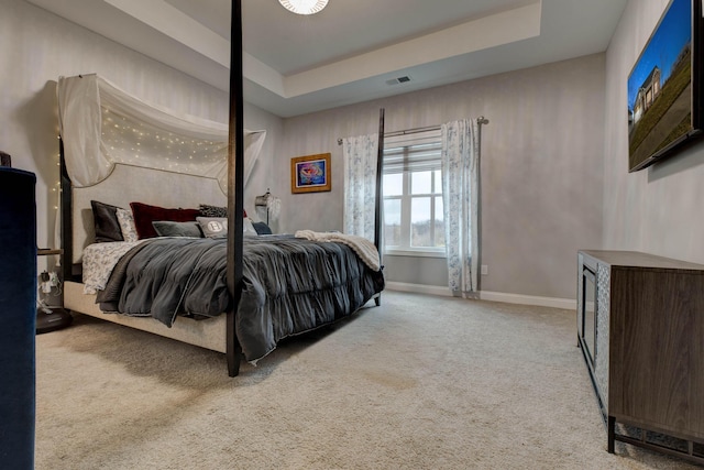 carpeted bedroom featuring a tray ceiling, visible vents, and baseboards