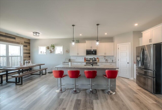 kitchen featuring stainless steel appliances, light wood-style flooring, a sink, white cabinetry, and a breakfast bar