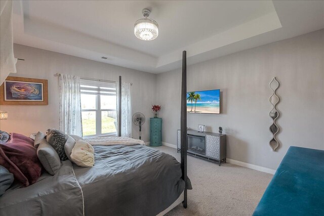 bedroom featuring light carpet, a tray ceiling, and baseboards