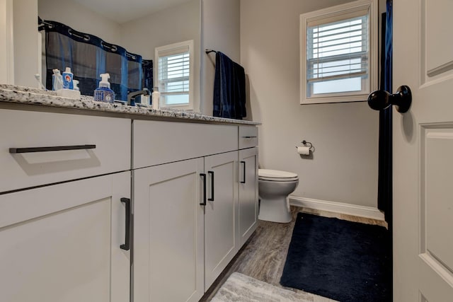 bathroom with a shower, toilet, vanity, wood finished floors, and baseboards