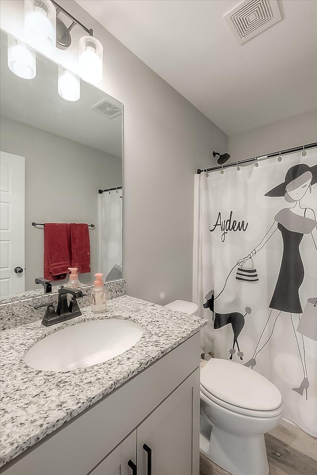 bathroom with toilet, vanity, wood finished floors, and visible vents