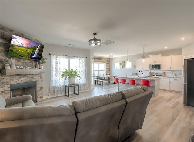 living room with a stone fireplace, light wood-type flooring, ceiling fan, visible vents, and recessed lighting