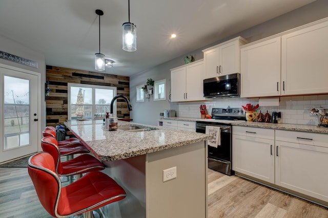 kitchen with wooden walls, light wood-style floors, black microwave, a sink, and range with electric stovetop