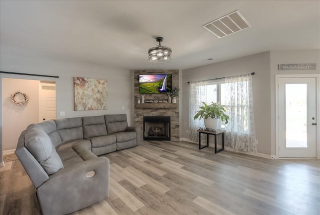 living room with baseboards, a stone fireplace, visible vents, and light wood-type flooring