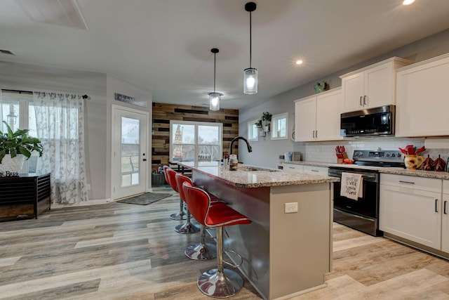 kitchen with a center island with sink, stainless steel microwave, black range with electric stovetop, light wood-type flooring, and a sink