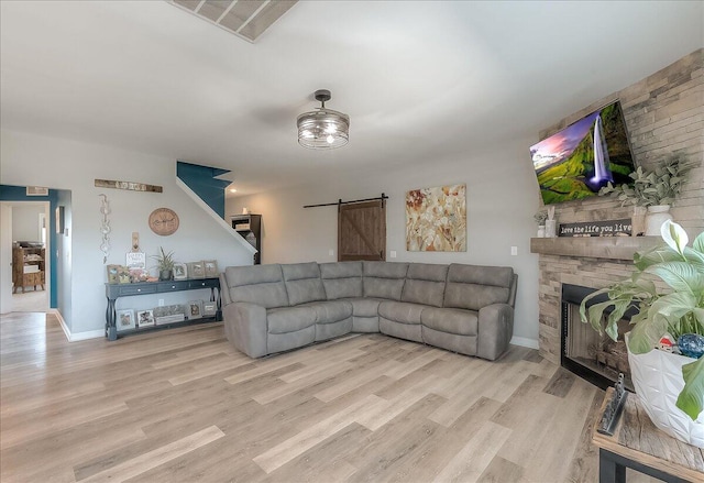 living room with a barn door, wood finished floors, a fireplace, and baseboards