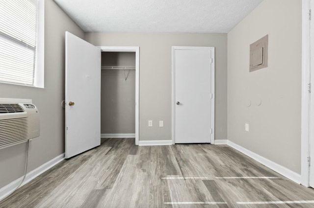 unfurnished bedroom with a closet, light hardwood / wood-style floors, a textured ceiling, and an AC wall unit