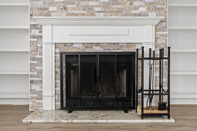 room details with built in shelves, wood-type flooring, and a tiled fireplace