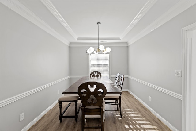 dining space featuring hardwood / wood-style floors, crown molding, a raised ceiling, and a chandelier