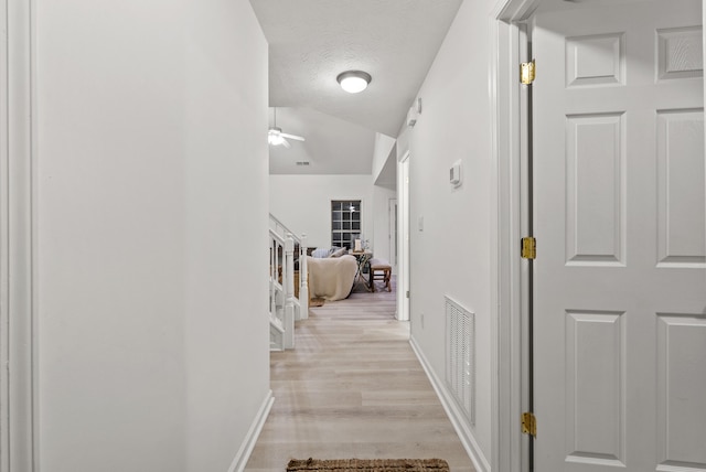 corridor with light wood-type flooring and a textured ceiling