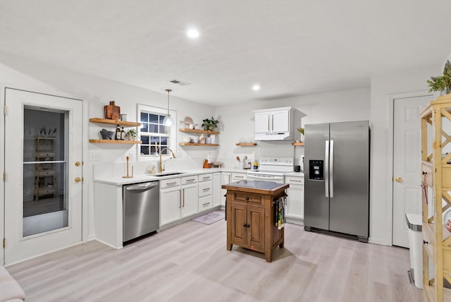 kitchen featuring decorative light fixtures, sink, white cabinets, stainless steel appliances, and light hardwood / wood-style flooring