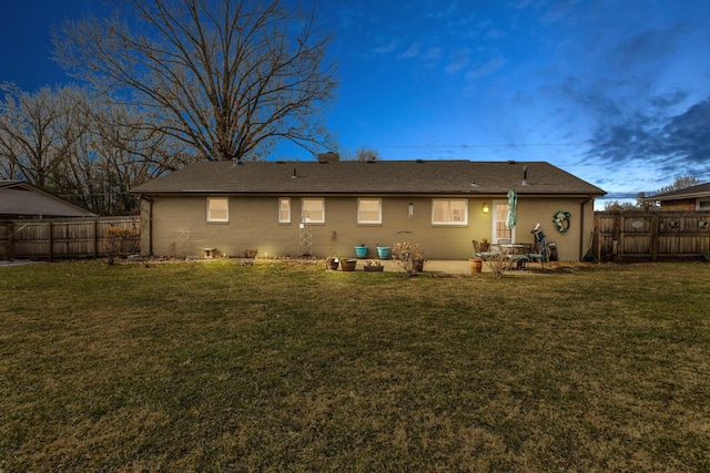 back house at dusk with a lawn and a patio