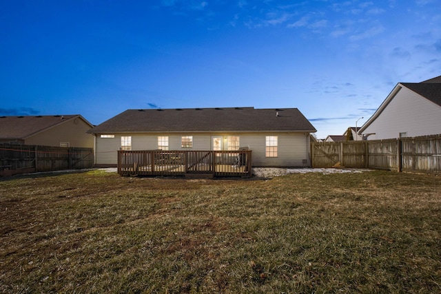 back house at dusk with a wooden deck and a lawn