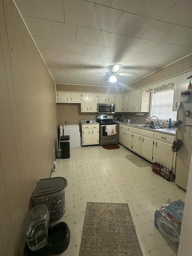 kitchen with appliances with stainless steel finishes, a sink, wooden walls, and light floors