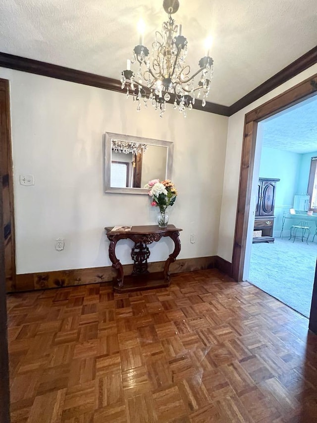 hall featuring a textured ceiling, baseboards, a chandelier, and crown molding