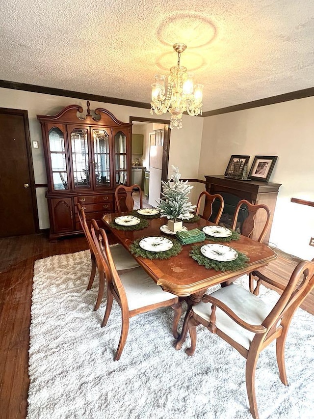 dining area with a textured ceiling, ornamental molding, a chandelier, and dark wood-style flooring