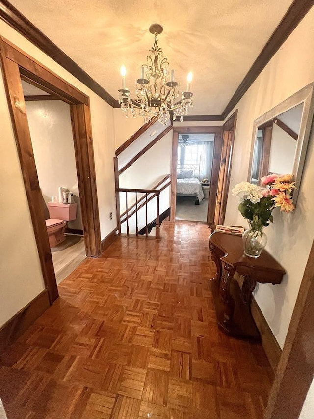 corridor with ornamental molding, a textured ceiling, baseboards, and an inviting chandelier