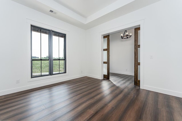 empty room featuring a tray ceiling, dark hardwood / wood-style floors, and a chandelier