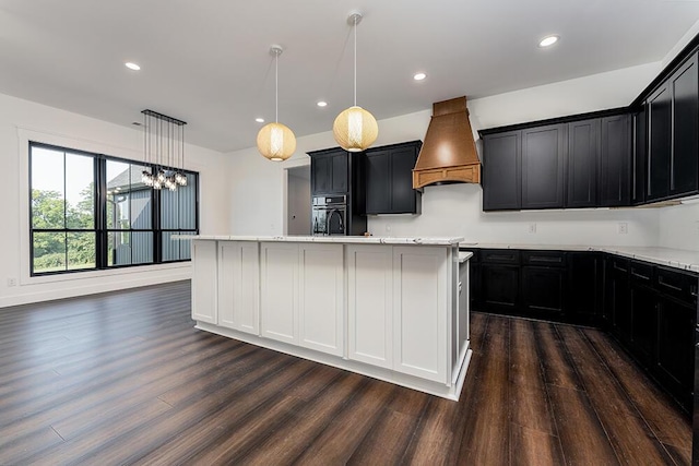 kitchen with dark hardwood / wood-style floors, decorative light fixtures, custom range hood, and a center island with sink