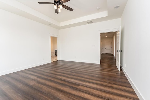 unfurnished room featuring ceiling fan, dark hardwood / wood-style flooring, and a tray ceiling