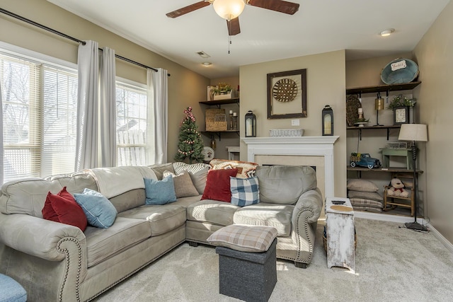 carpeted living area with ceiling fan, a fireplace, baseboards, and visible vents