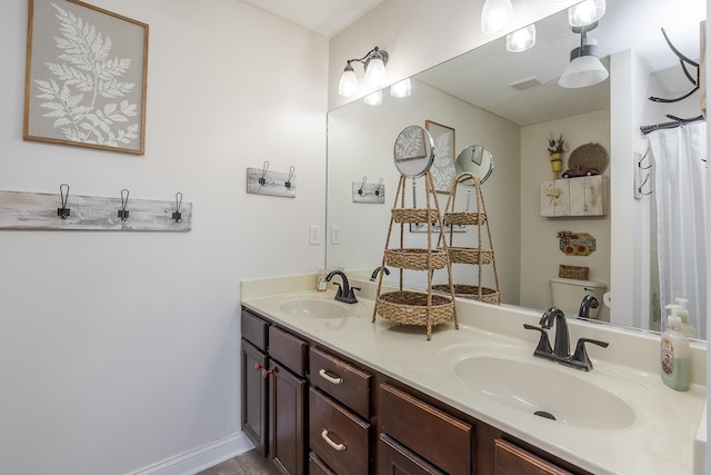 bathroom with toilet, double vanity, a sink, and visible vents