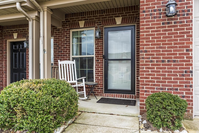 entrance to property featuring a porch and brick siding