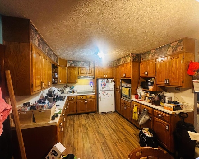 kitchen with white refrigerator, oven, a textured ceiling, and light hardwood / wood-style flooring