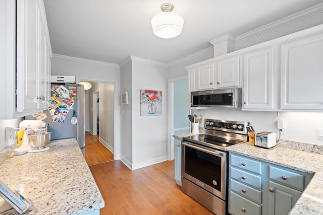 kitchen featuring white cabinetry, light wood-type flooring, ornamental molding, appliances with stainless steel finishes, and light stone countertops