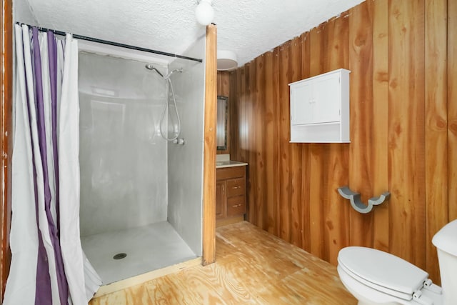 bathroom featuring vanity, a textured ceiling, a shower with curtain, toilet, and wood walls