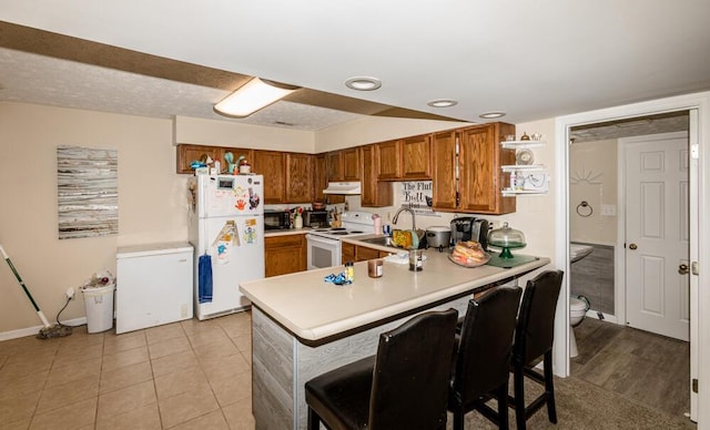 kitchen with sink, a kitchen bar, light tile patterned floors, kitchen peninsula, and white appliances