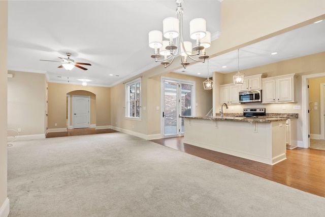 kitchen with stone countertops, decorative light fixtures, light carpet, stainless steel appliances, and ceiling fan with notable chandelier