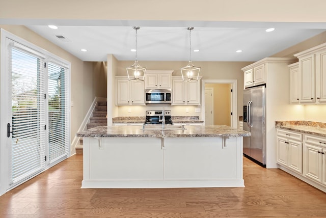 kitchen featuring a breakfast bar, a center island with sink, hanging light fixtures, light hardwood / wood-style flooring, and stainless steel appliances