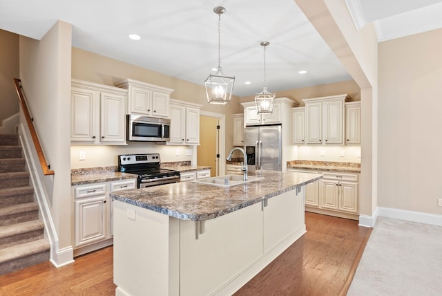 kitchen with a kitchen island with sink, sink, stainless steel appliances, and hanging light fixtures