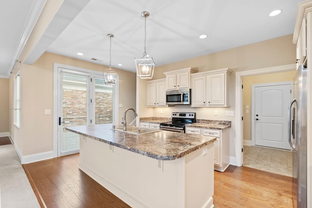 kitchen with a kitchen bar, sink, hanging light fixtures, appliances with stainless steel finishes, and a kitchen island with sink