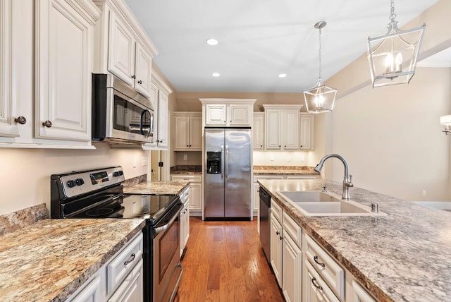 kitchen featuring sink, hardwood / wood-style floors, stainless steel appliances, light stone counters, and decorative light fixtures