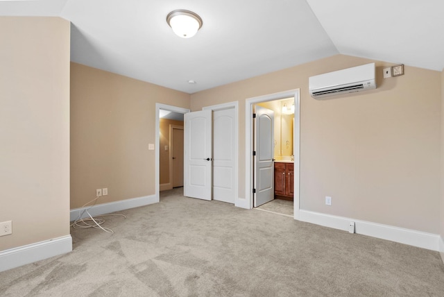 unfurnished bedroom featuring ensuite bathroom, light carpet, a wall mounted air conditioner, and lofted ceiling