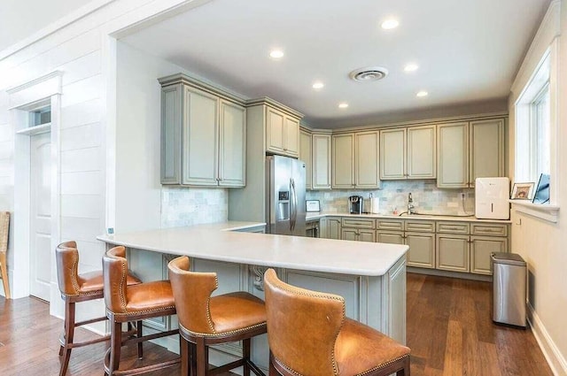 kitchen featuring backsplash, a kitchen breakfast bar, stainless steel refrigerator with ice dispenser, dark hardwood / wood-style flooring, and kitchen peninsula