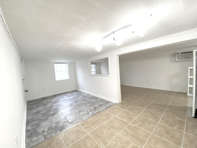 basement with a wall mounted AC, track lighting, and a textured ceiling