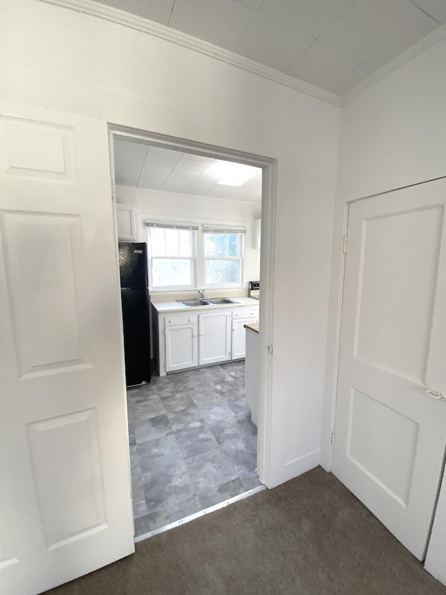 kitchen with ornamental molding, black refrigerator, sink, and white cabinets