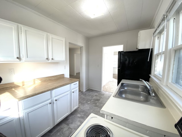 kitchen with sink, ornamental molding, white cabinets, and black fridge