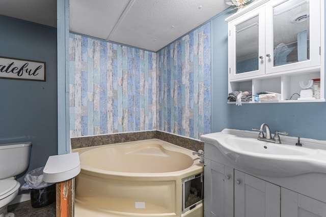 bathroom featuring vanity, a bath, a textured ceiling, and toilet