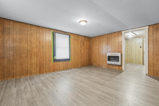 unfurnished living room featuring wooden walls, heating unit, and light hardwood / wood-style floors