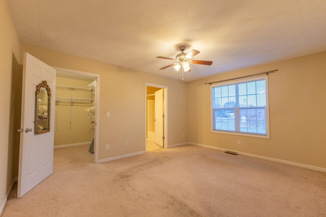 unfurnished bedroom featuring ensuite bathroom, a spacious closet, light colored carpet, a closet, and ceiling fan