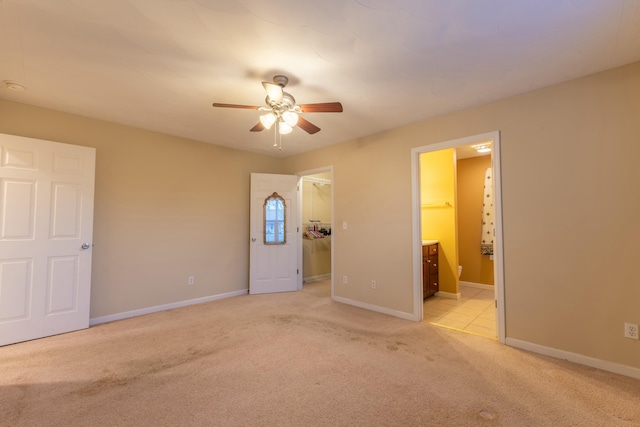 unfurnished bedroom featuring ensuite bathroom, a walk in closet, light colored carpet, ceiling fan, and a closet